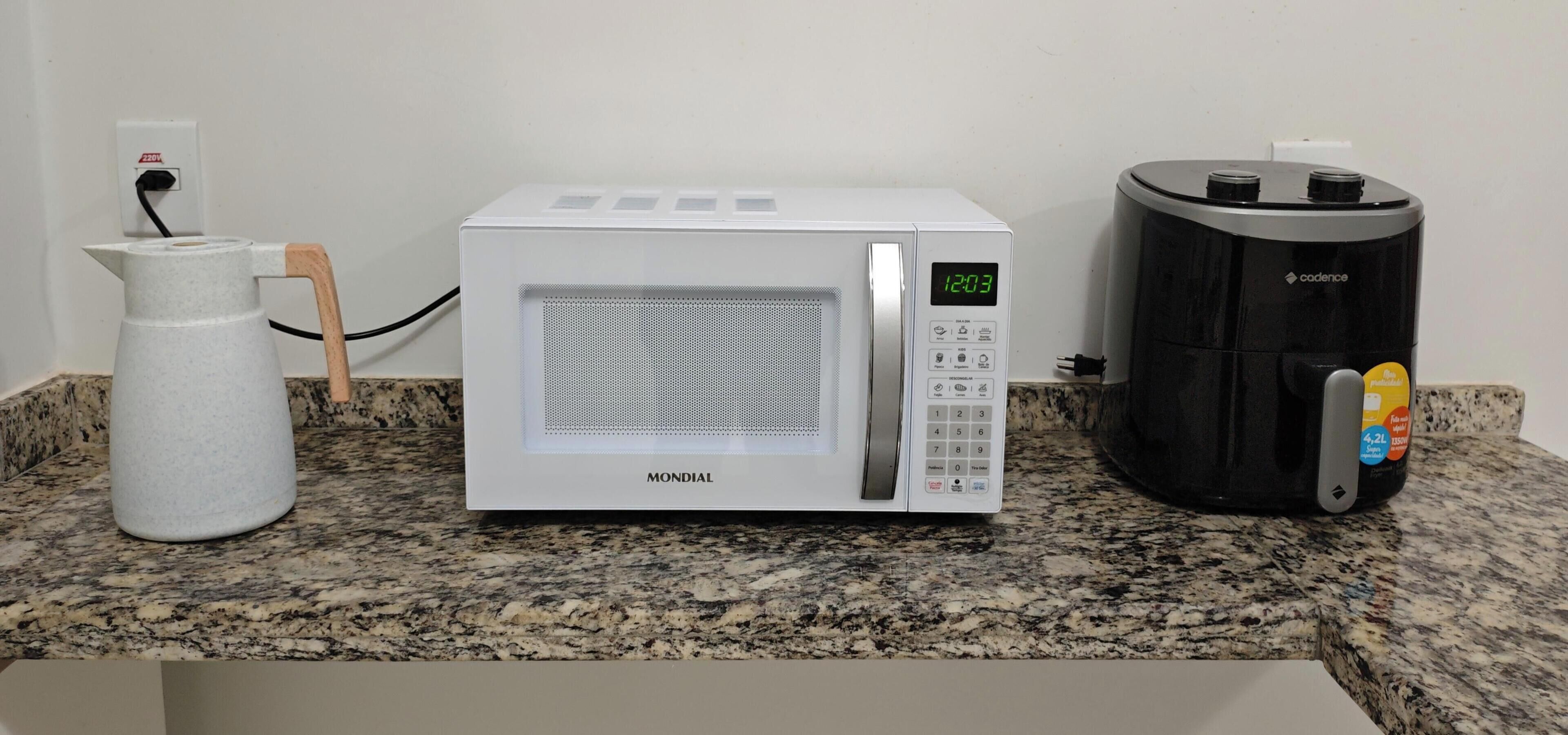 A kitchen with a white microwave, a coffee maker, and a water dispenser on a granite countertop.