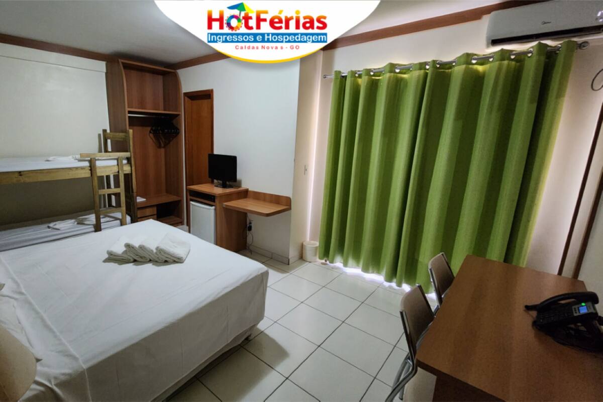 Une chambre d’hôtel avec un lit, un bureau, une chaise, une télévision et un rideau vert.