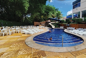 Uma área de piscina com espreguiçadeiras e um escorregador, cercada por um muro de pedra e vegetação.