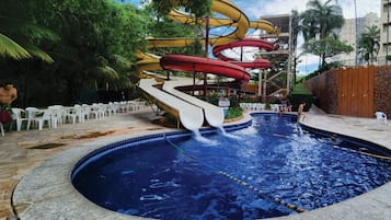 A swimming pool with multiple water slides, surrounded by palm trees and a stone wall.