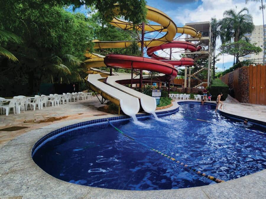 A swimming pool with multiple water slides, surrounded by palm trees and a stone wall.