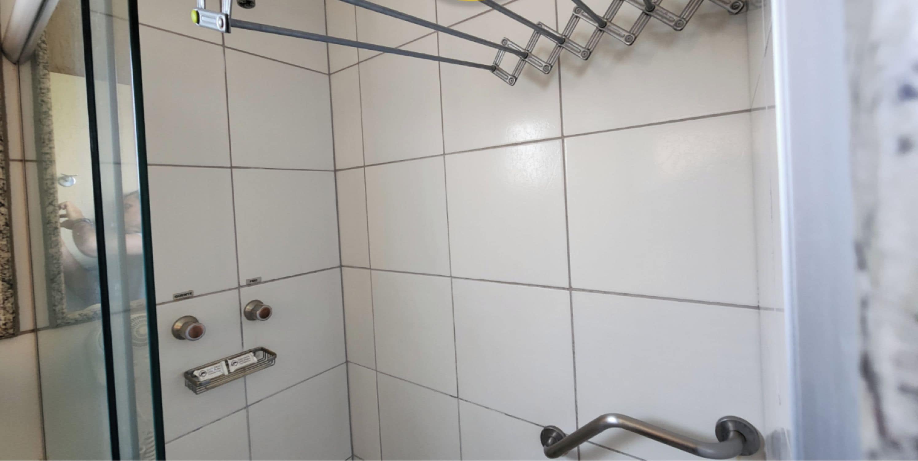 A corner of a bathroom with white tiles, a glass shower enclosure, a metal grab bar, and a towel rack.
