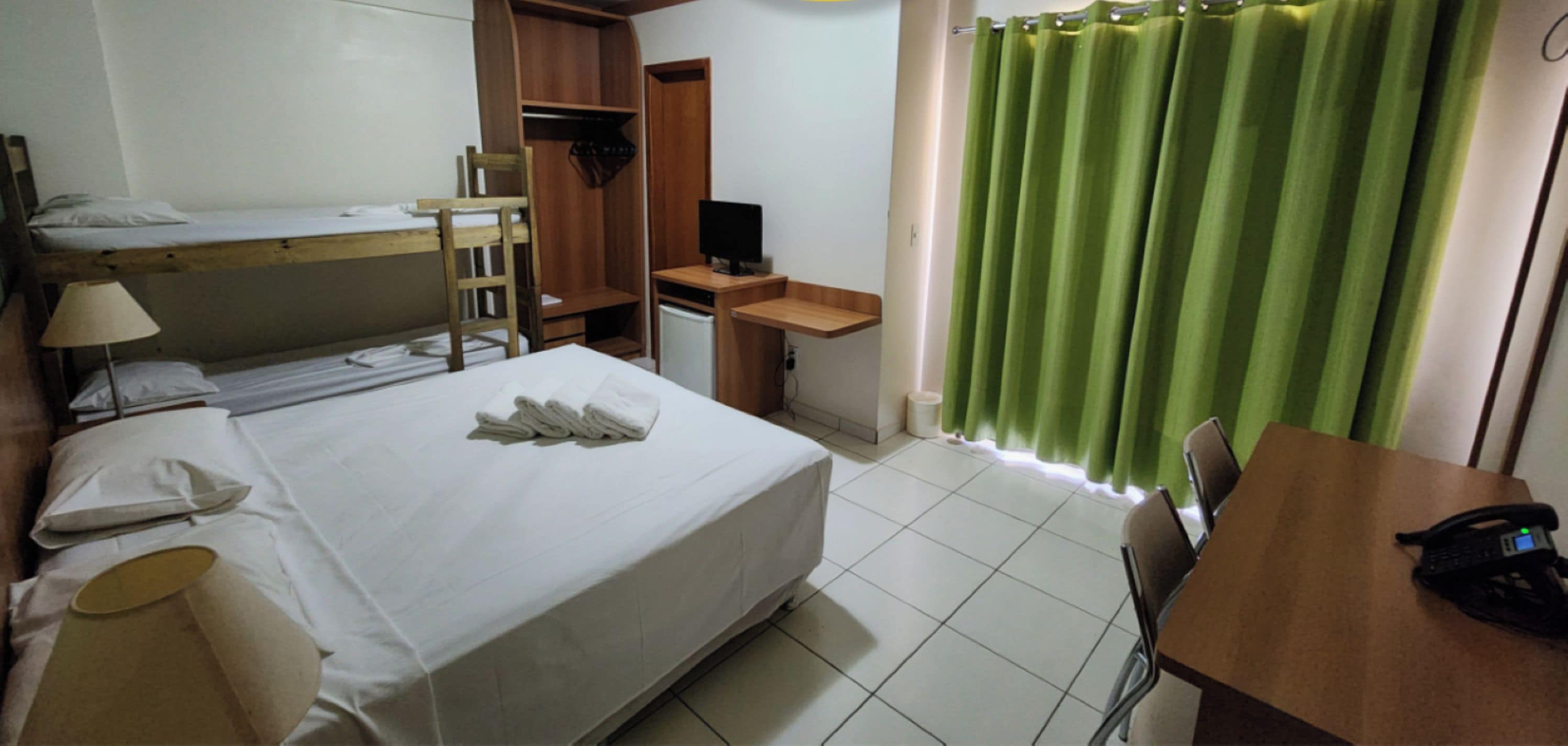 Una habitación de hotel con una cama, un escritorio, una silla, un televisor y una cortina verde.