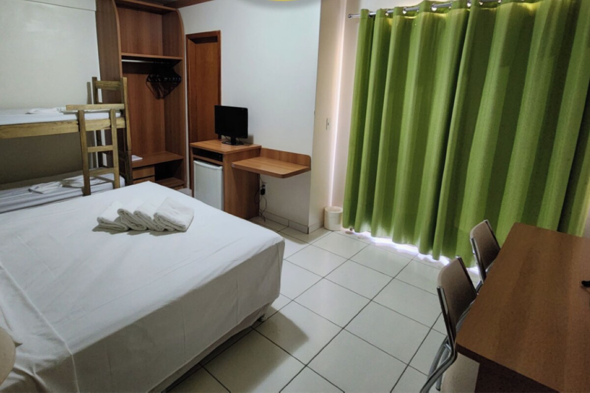 A hotel room with a bed, a desk, a chair, a TV, and a green curtain.