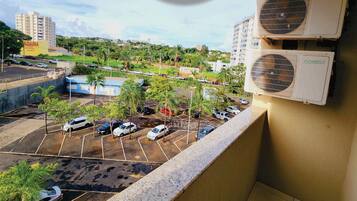 A view from a balcony overlooking a parking lot with several cars, palm trees, and buildings in the background.