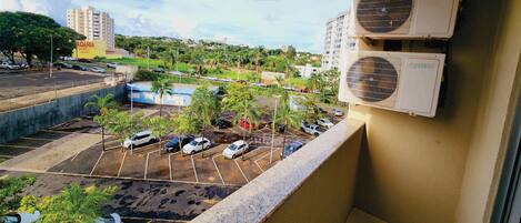 A view from a balcony overlooking a parking lot with several cars, palm trees, and buildings in the background.