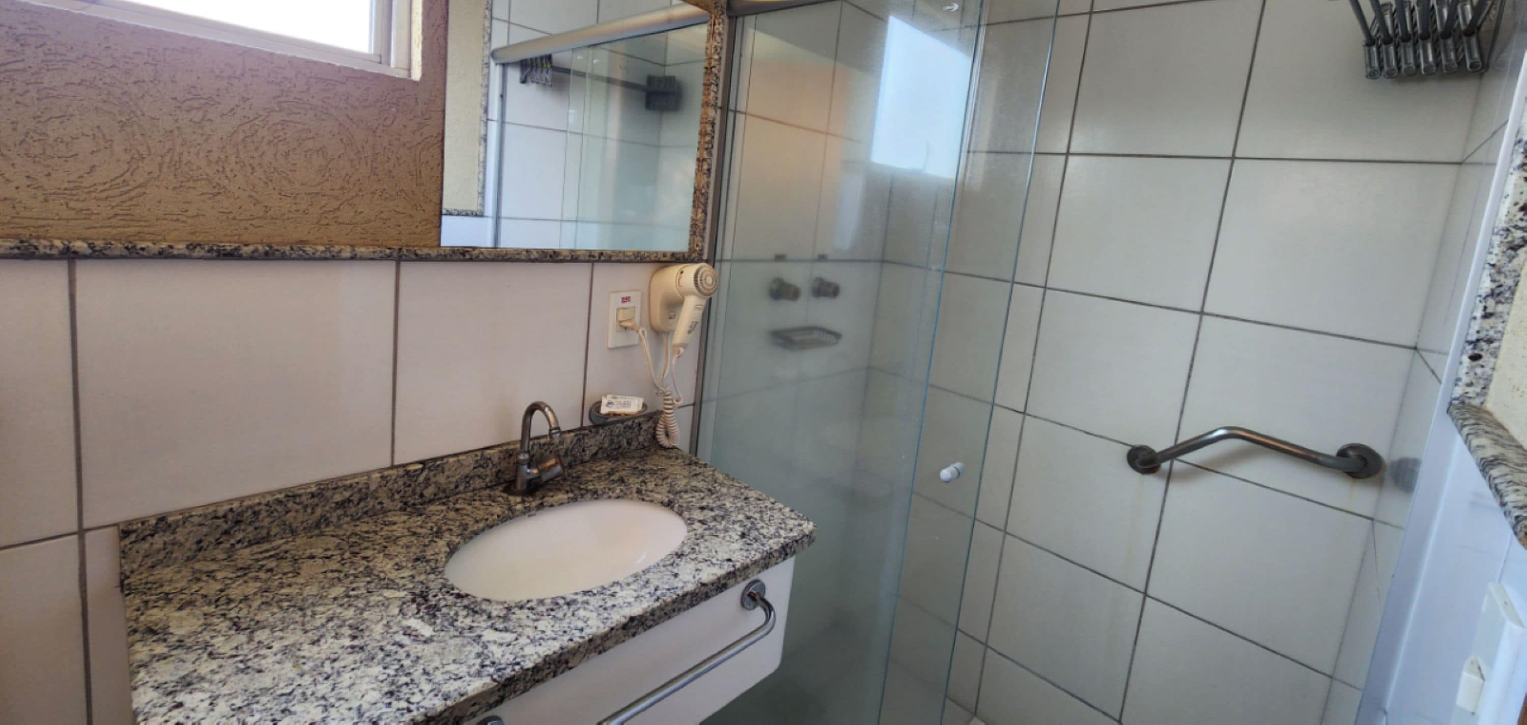 A bathroom with a granite countertop sink, a mirror, and a glass shower enclosure.
