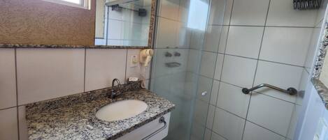 A bathroom with a granite countertop sink, a mirror, and a glass shower enclosure.