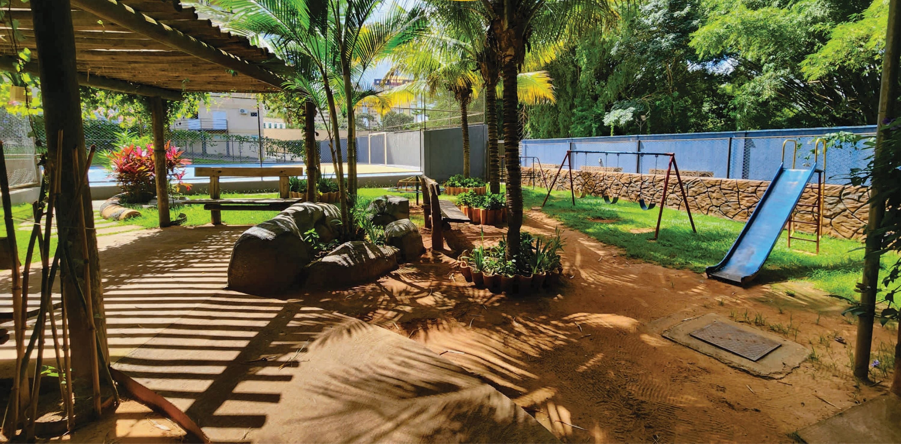 A covered outdoor area with a dirt path, palm trees, a swing set, and a slide.