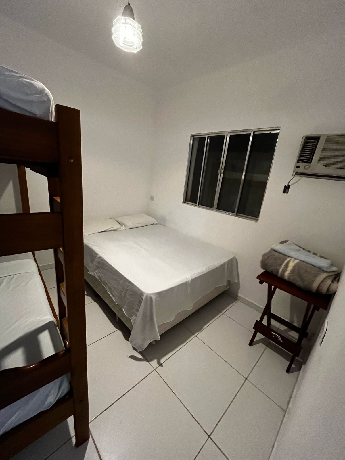 Una habitación pequeña y limpia con una cama alta, una cama individual, una ventana y un calentador.