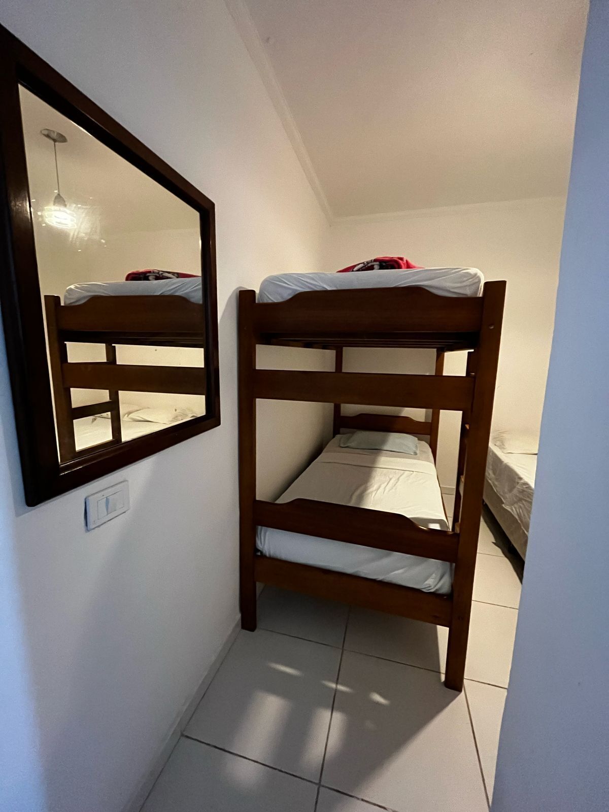 A small, narrow room with two bunk beds, a mirror, and a light switch on the wall.