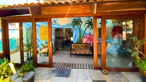 A covered outdoor seating area with a mural, potted plants, and a tiled floor. - Pousada Ilha Bonita (Guarujá)