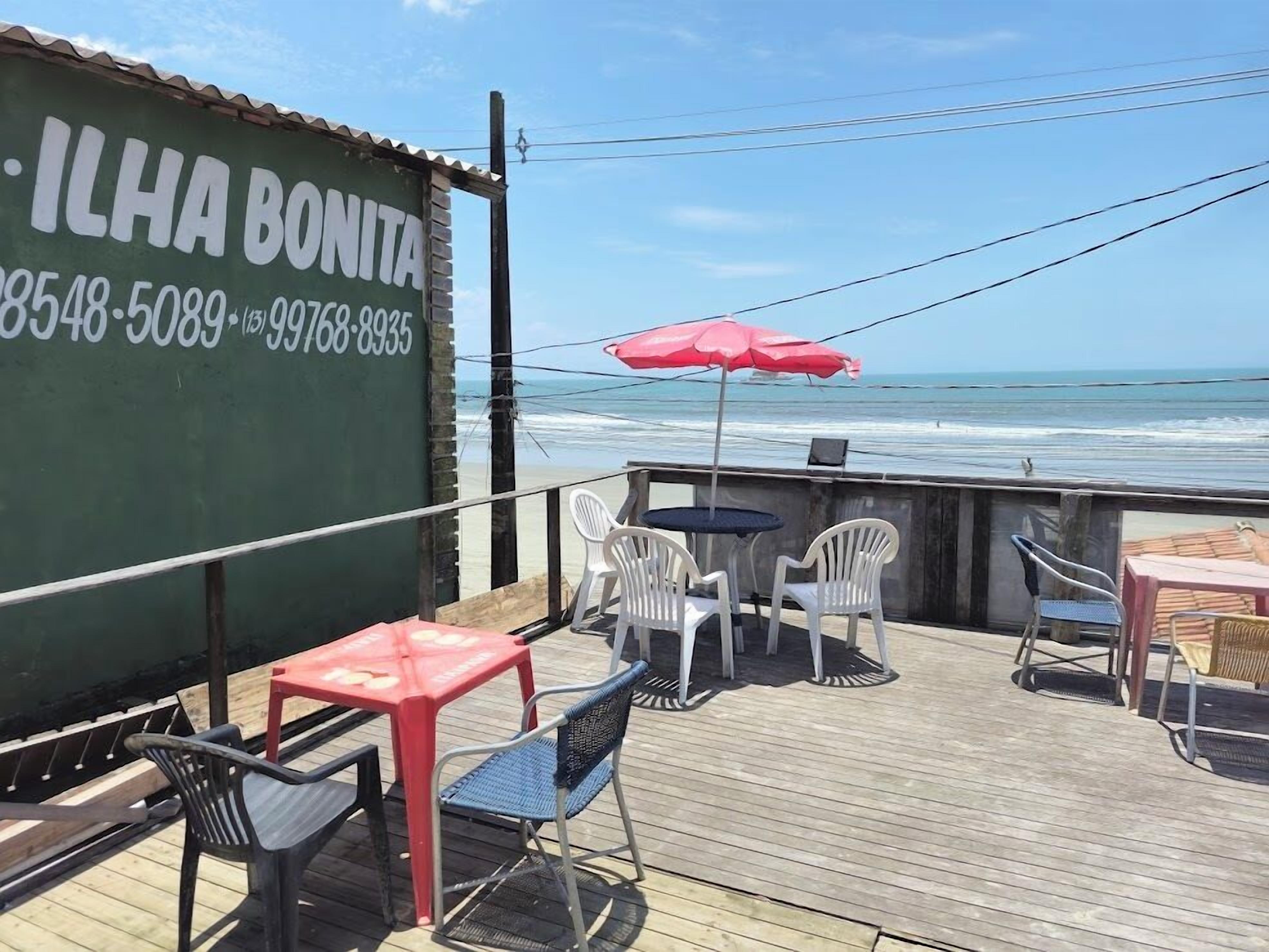 A seaside patio with outdoor seating, a green wall with contact information, and a view of the ocean.