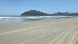 A beach with a sandy shore and a small hill in the background. - Pousada Ilha Bonita (Guarujá)
