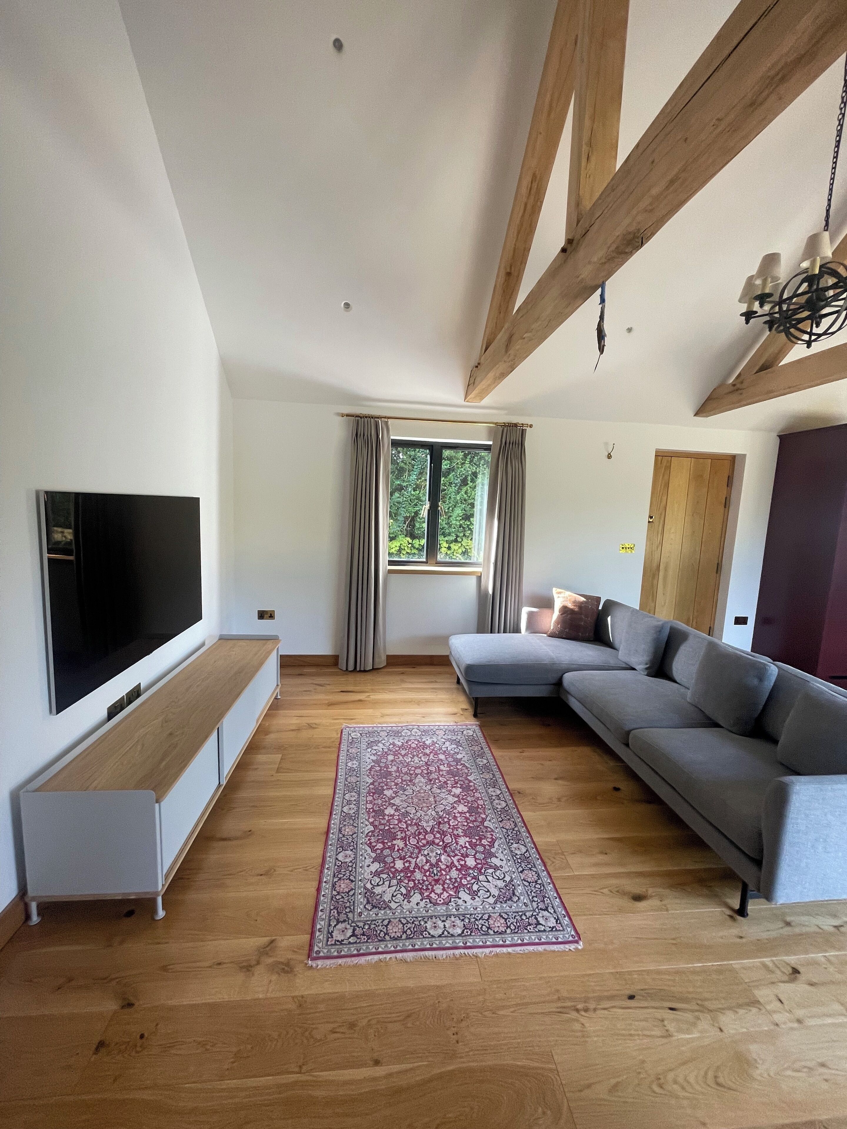 A modern living room with a large flat-screen TV, a grey sectional sofa, a wooden bench, and a patterned rug.