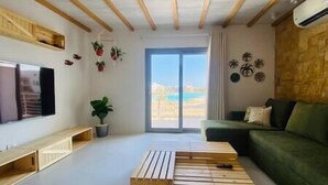 A modern living room with a wooden coffee table, a green sofa, and a large window offering a view of the outdoors. - Rustic 1 BR-Apt@ Swanlake - El Gouna (Second Hurghada)