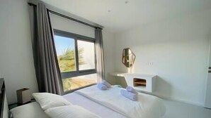 A modern hotel room with a large bed, a bedside table with a lamp, and a window with curtains. - Rustic 1 BR-Apt@ Swanlake - El Gouna (Second Hurghada)