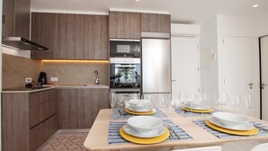 Una cocina moderna con armarios de madera, horno empotrado y comedor preparado para seis personas, con platos amarillos y vasos transparentes.