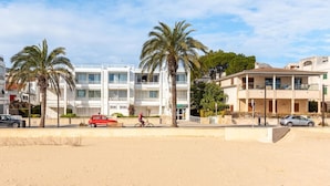 Un edificio costero con balcones, palmeras y una playa arenosa al frente.