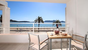 Un balcón con una mesa lista para dos personas, con vista a una playa con palmeras y montañas a lo lejos.