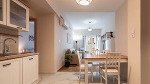 A modern kitchen with white cabinets, a marble floor, and a dining area with a wooden table and white chairs. - Rovertou Galli 3-5, By Athens Concept Residences (Athina)
