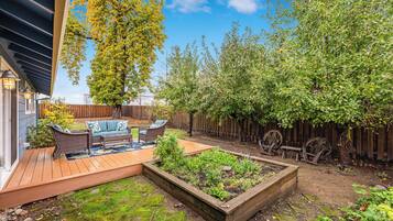 Eine Holzterrasse mit Gartenmöbeln, einem erhöhten Blumenbeet und einem Holzzaun.