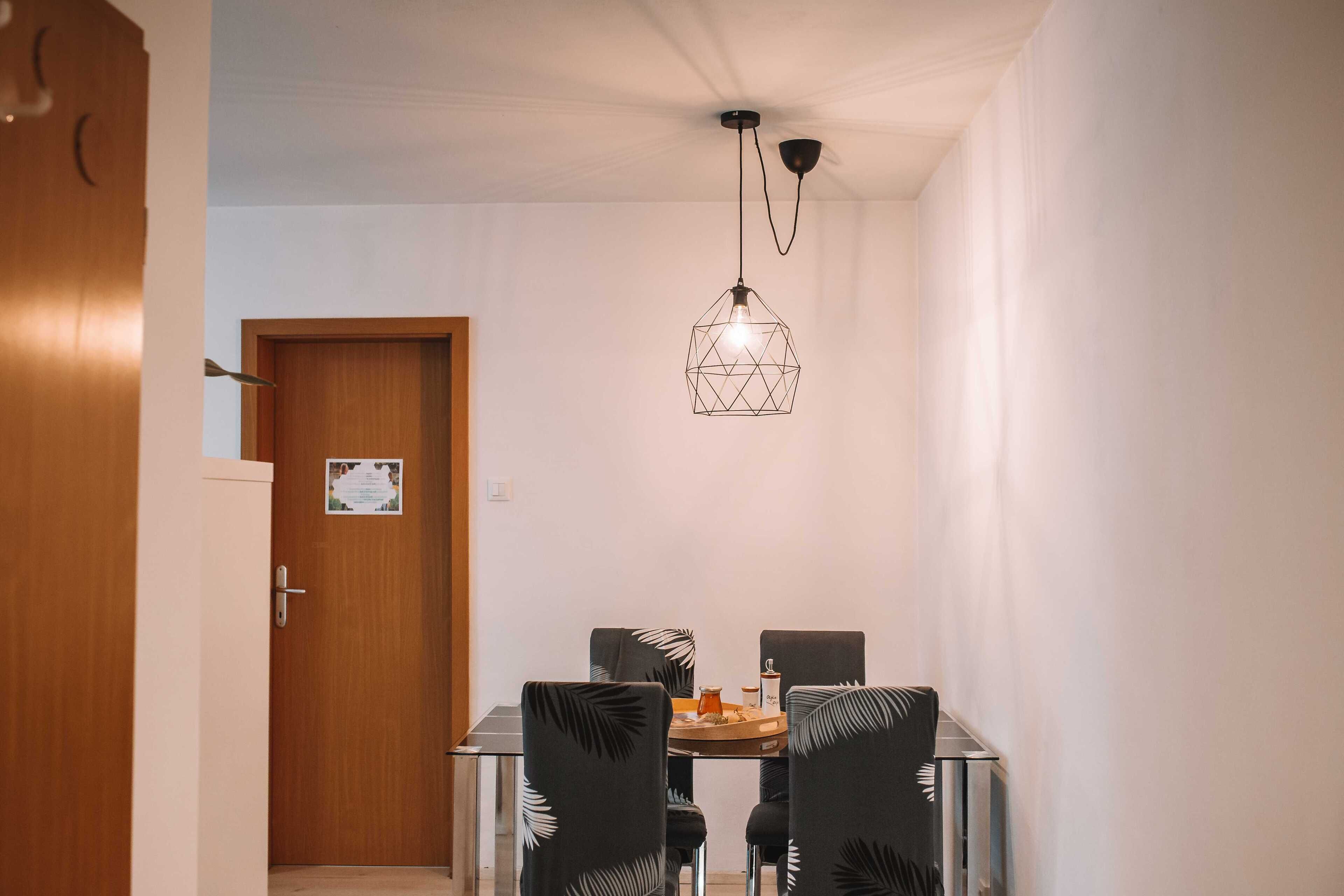 A dining area with a wooden door, a glass table, and four chairs with a leaf pattern.