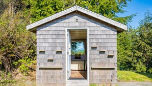 A small wooden cabin with a door open, revealing a bed inside.