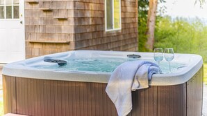 A hot tub with two glasses of water, a towel, and a wooden deck.