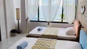 A hotel room with two beds, a ceiling fan, a window with curtains, and a bedside lamp.