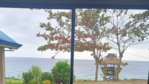 Eine Küche mit Spüle und Fenster mit Blick auf einen Strand mit einem Gebäude mit Reetdach.