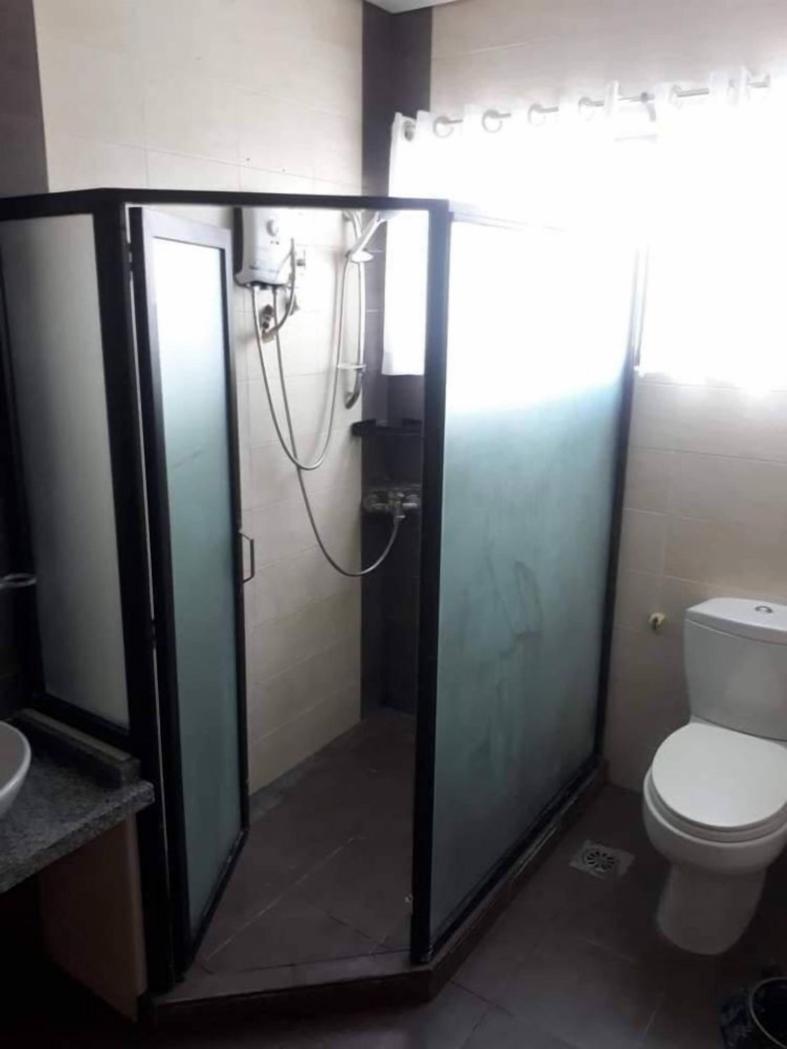 Um banheiro com chuveiro em box de vidro, vaso sanitário e pia.