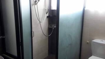 Um banheiro com chuveiro em box de vidro, vaso sanitário e pia.