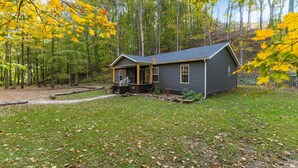 A cabin with a porch, surrounded by a forest with autumn foliage.