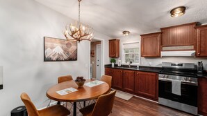 A modern kitchen with wooden cabinets, a stainless steel stove, and a dining area with a round table and chairs.