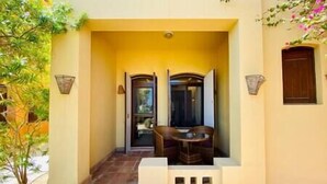 A building entrance with a wooden bench and a table, a small garden area, and a door leading inside.
