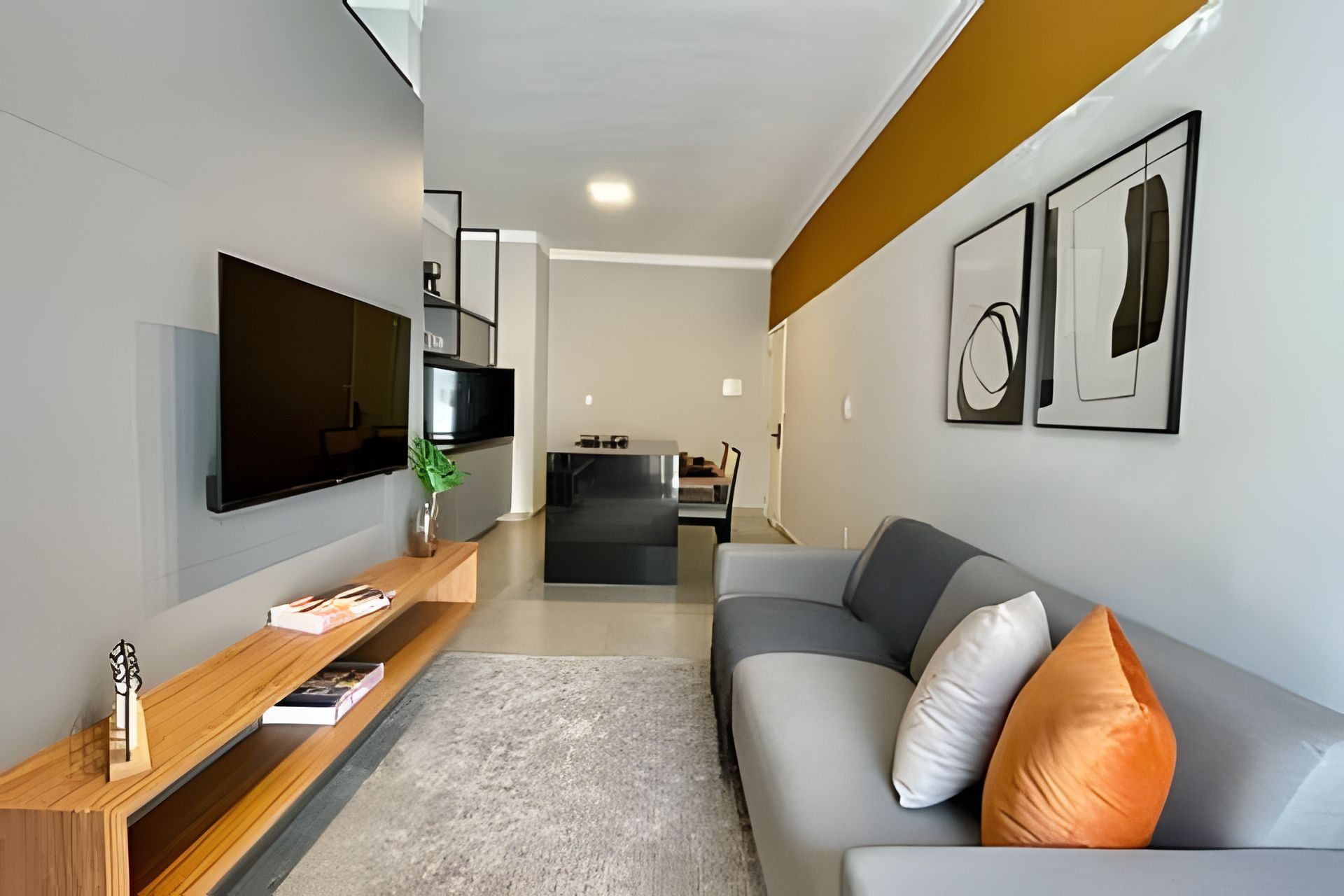 A modern living room with a flat-screen TV, wooden entertainment unit, grey sofa, and abstract wall art.