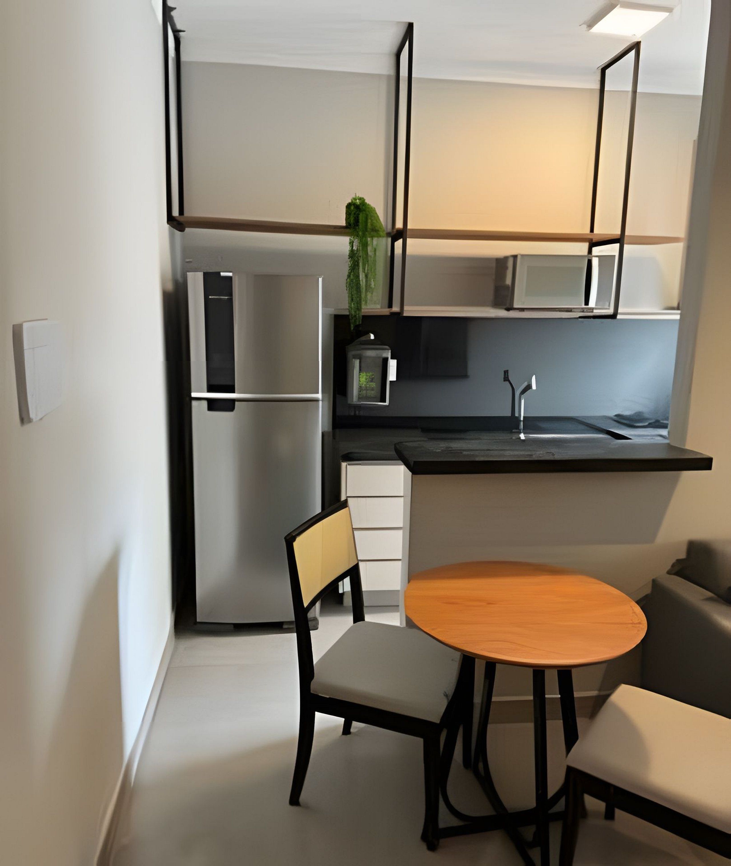 A compact kitchen with a refrigerator, microwave, and sink. There is a small dining table with two chairs.