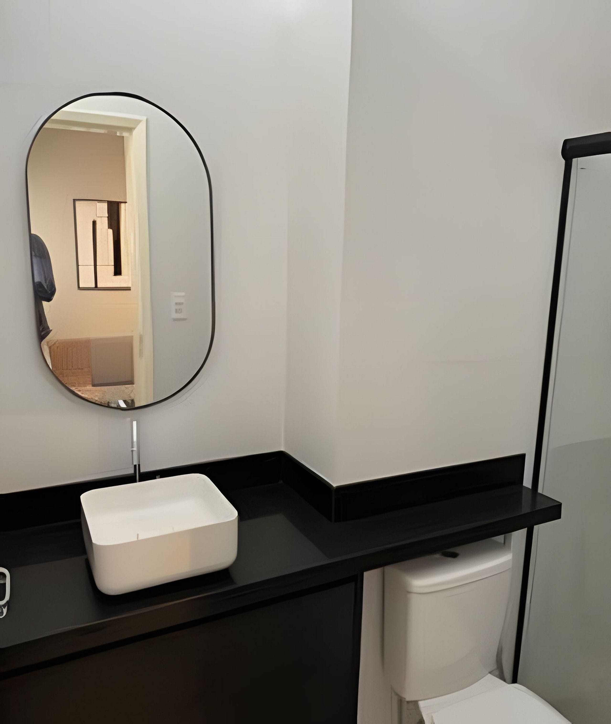 A modern bathroom with a black countertop, a white sink, and a mirror.