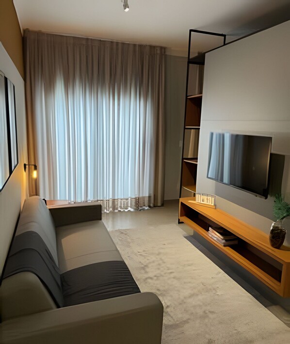 Uma sala de estar moderna com um sofá, uma TV de tela plana, um rack de madeira e uma janela grande com cortinas.