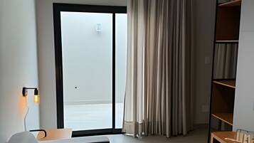 Quarto de hotel moderno com sofá, mesa lateral de madeira, estante embutida e porta de vidro deslizante que dá para uma varanda.