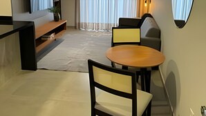Een moderne woonkamer met een bank, een eettafel met stoelen, een aan de muur bevestigde televisie en een groot raam met gordijnen.