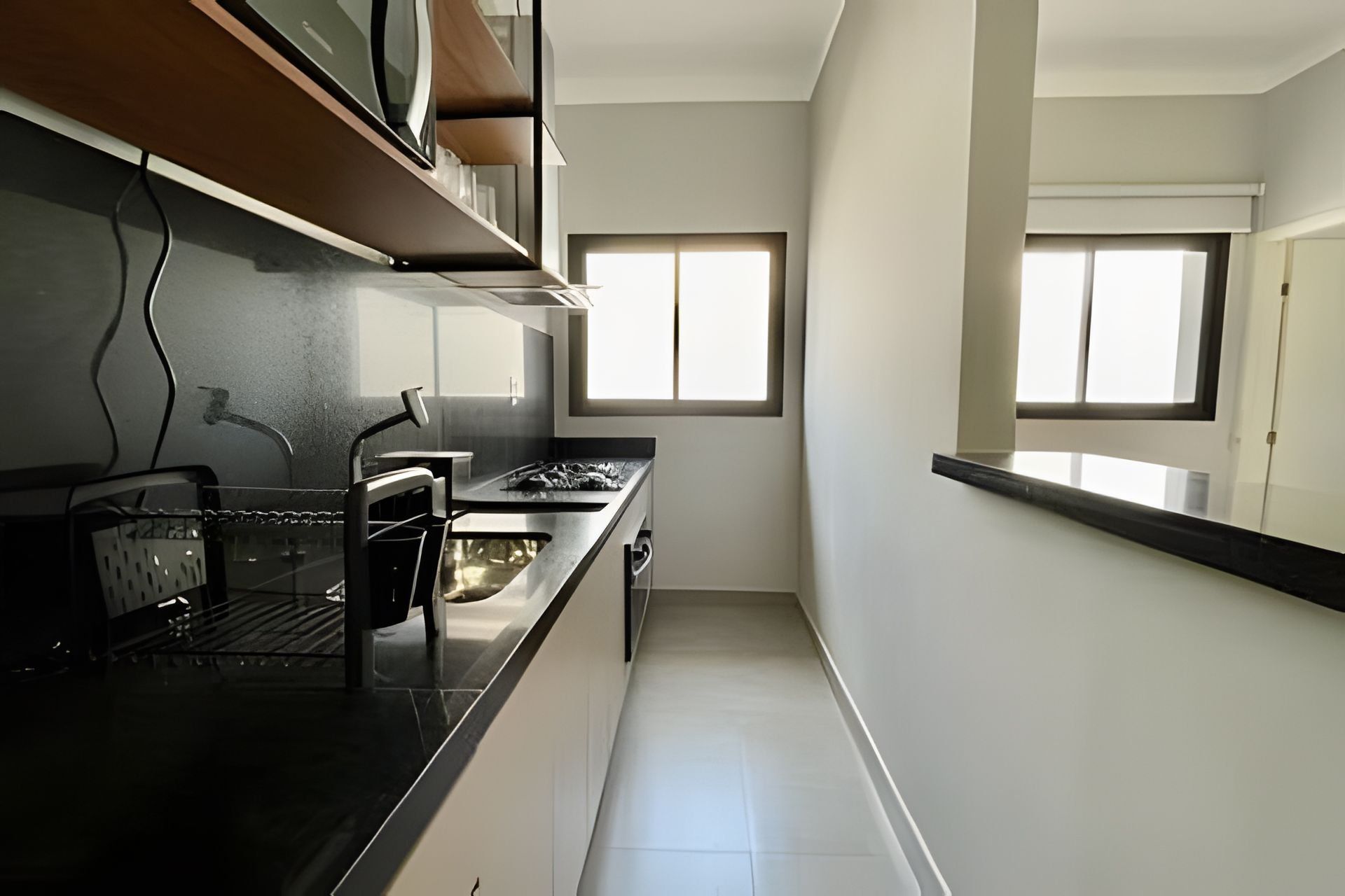 Una cocina estrecha con encimera negra, electrodomésticos de acero inoxidable y una ventana que proporciona luz natural.