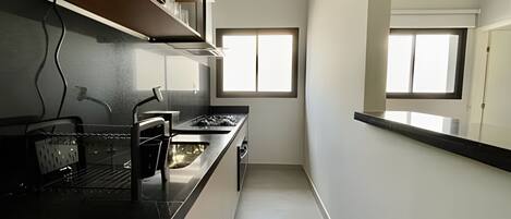 Una cocina estrecha con encimera negra, electrodomésticos de acero inoxidable y una ventana que proporciona luz natural.