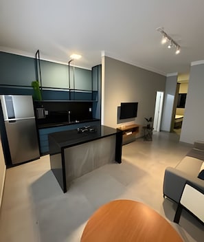 A modern kitchen with a built-in oven, a dining area with a wooden table, and a grey sofa. - MY STUDIO  (Franca)