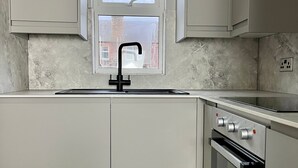 A modern kitchen with a built-in oven, a stainless steel sink, and a window above the sink. - Victoria Street (Galashiels)