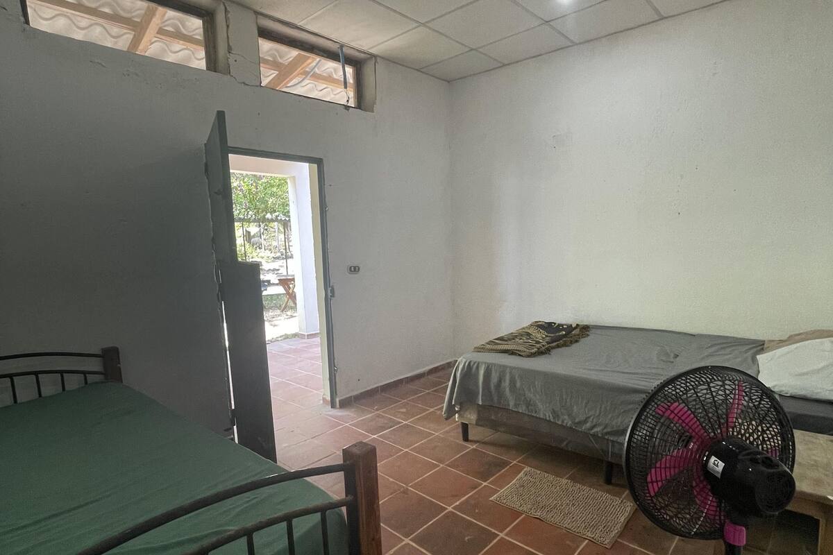 Een kamer met een bed, een ventilator en een deur naar buiten.