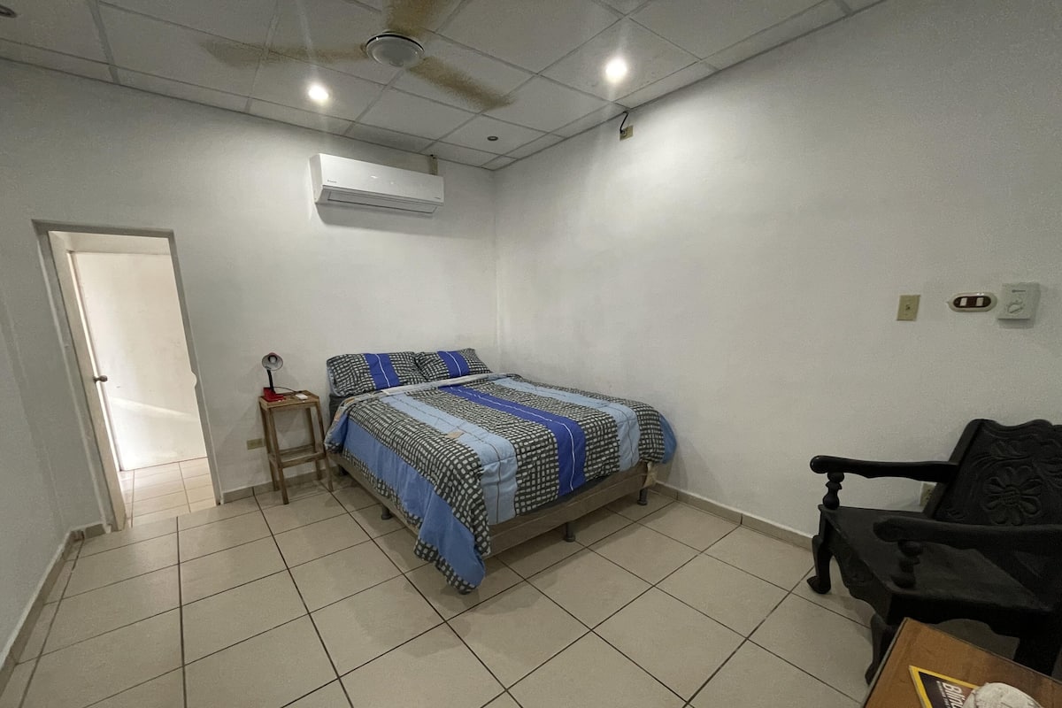Een slaapkamer met een bed, een stoel, een klein tafeltje en een airconditioner.