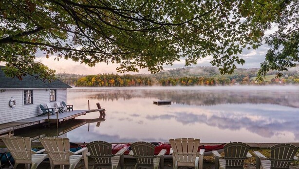 A lakeside cabin with a dock and chairs facing the water, surrounded by trees and a misty lake. - The Pines at Center Harbor (Moultonborough)