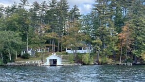 A dock with a small white building, surrounded by dense trees and houses in the background. - The Pines at Center Harbor (Moultonborough)